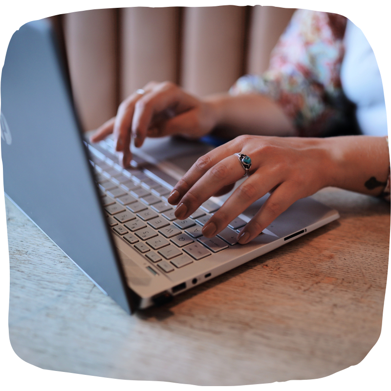 Close-up photo of a woman typing on a laptop. She's wearing a blue ring on her middle finger. We can't see her face.